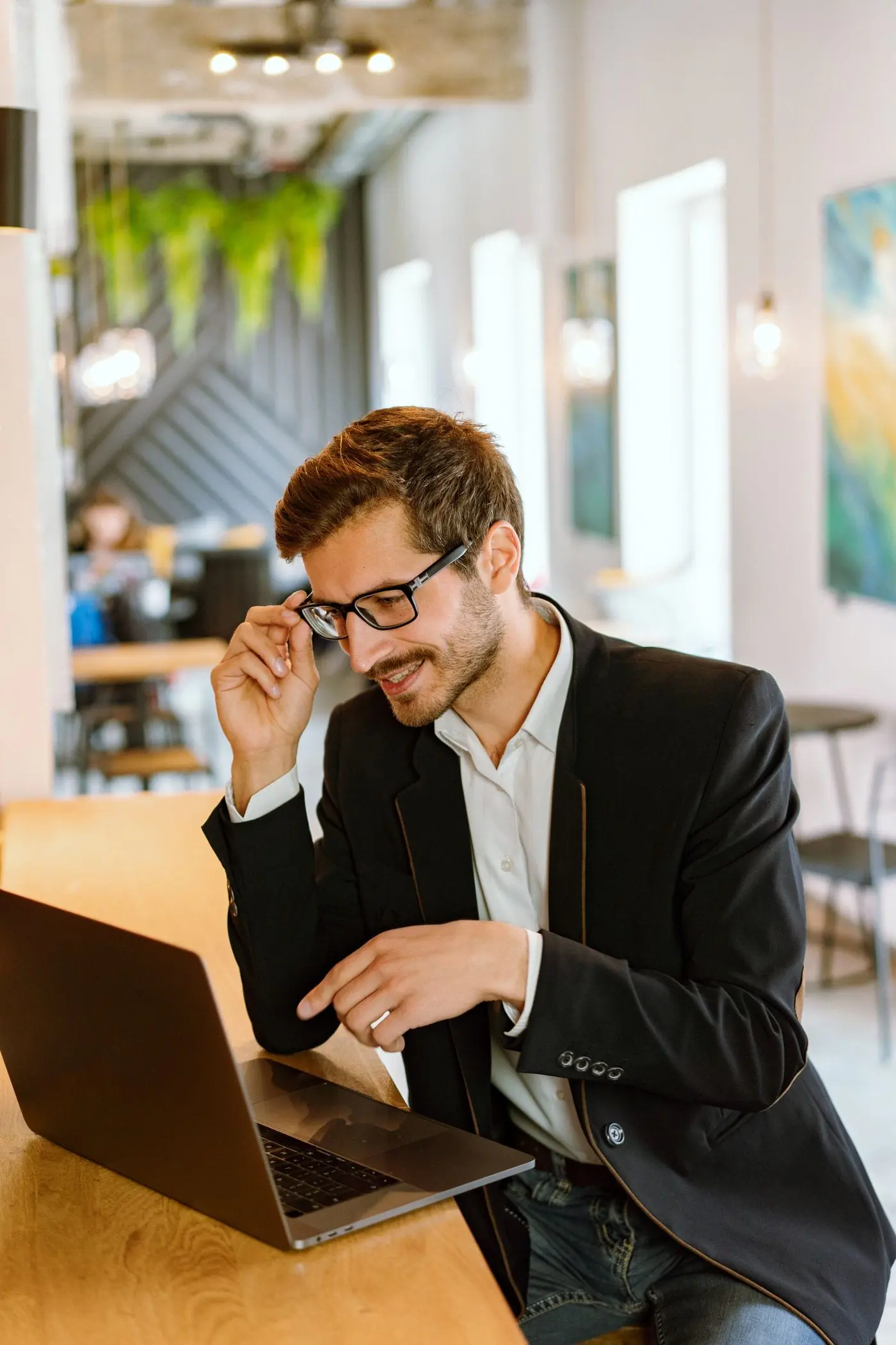 A consultant in glasses and a dark blazer smiling at his laptop