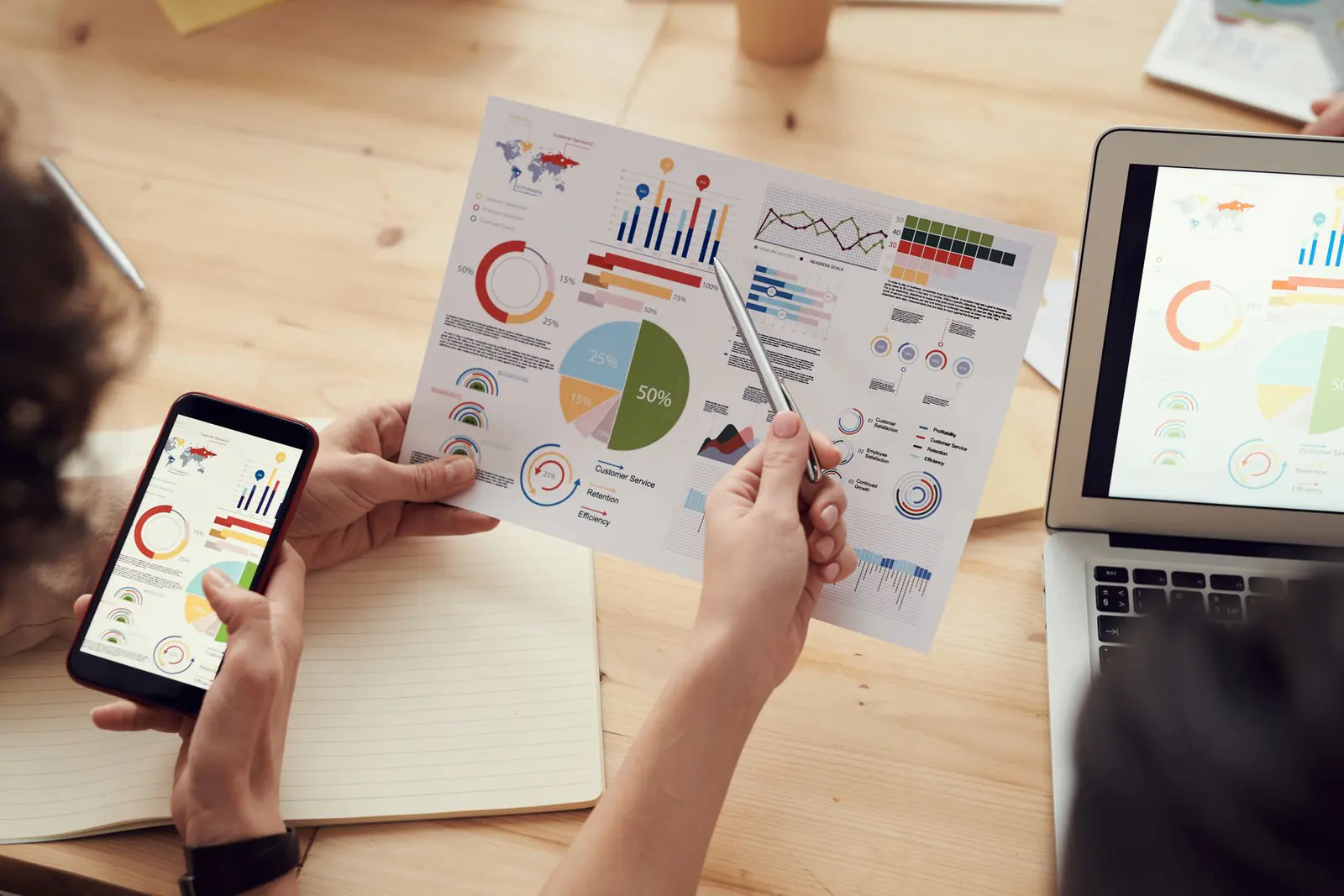 Hands holding a printed chart and a phone over a laptop