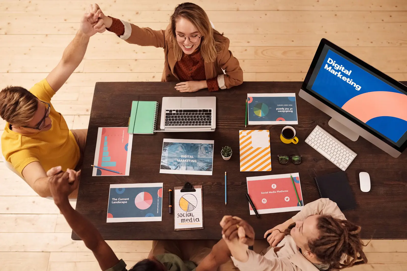 Four people round a table of printed marketing reports, high-fiving