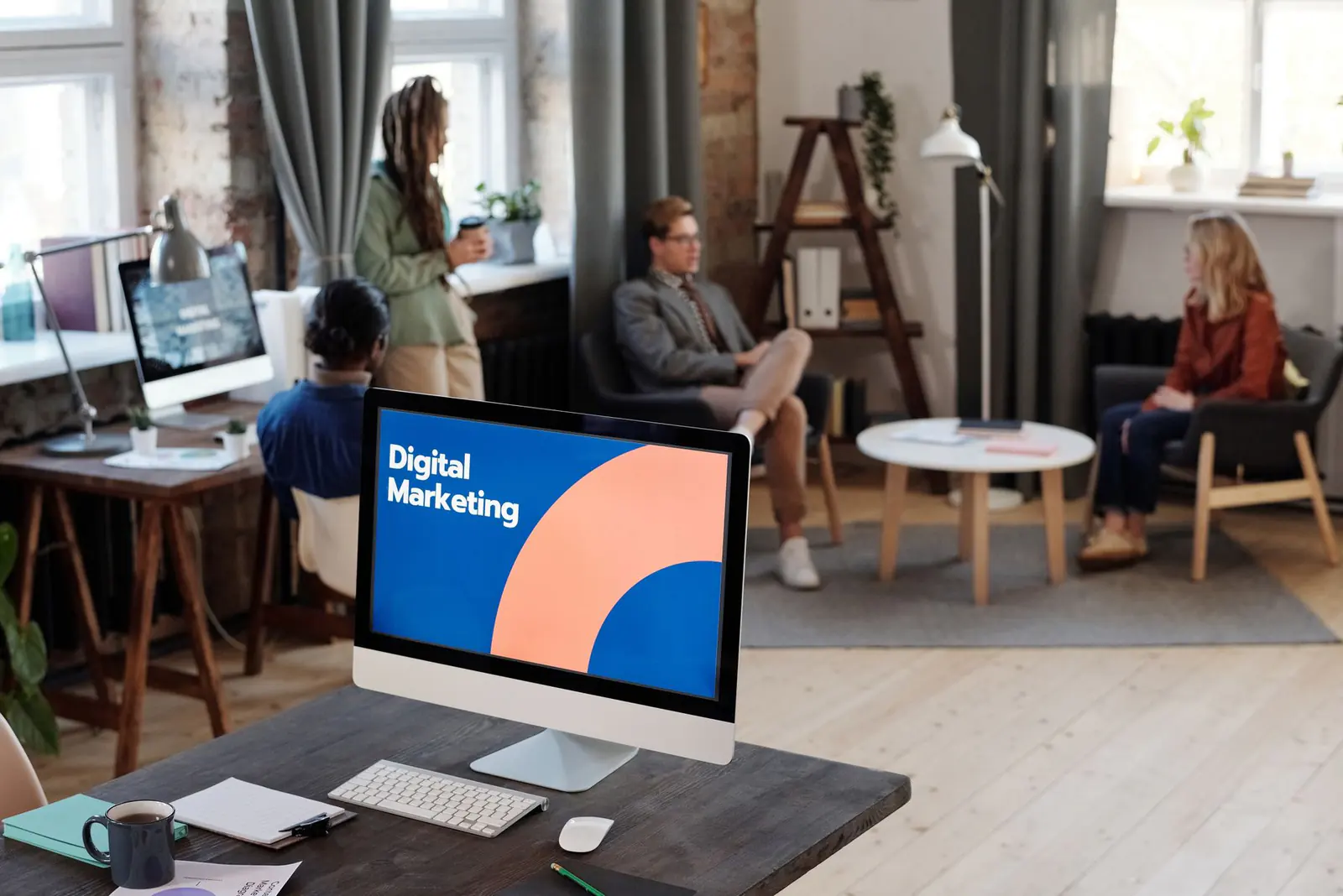 An office with a desktop screen in front and people talking in the background